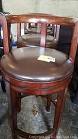 Front view of four round wooden low back bar stools showing the padded dark brown seats and curved backrest.