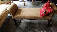 Photo showing side view of upholstered bench with rolled arms and red cushion on top.