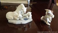 Two porcelain figurines displayed on a dark surface: polar bears group and cat with mouse