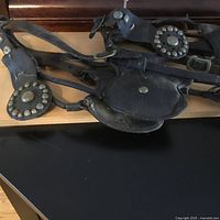 Close-up photo of black leather driving bridle with round brass studs and decorative brass fittings lying on black table.