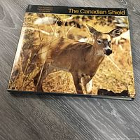 Hardcover book titled The Canadian Shield showing a deer in a natural setting, placed on a floor.