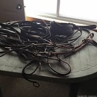 Multiple dark leather horse halters, bridles with reins, and harness spread on a plastic table showing various buckles and straps.