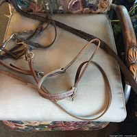Miscellaneous brown leather horse bridle with reins, placed on a beige cushioned chair.
