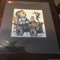 Print of child sitting in wooden wagon with bird perched on side, colorful details and floral accents, mounted on black matte board and sealed in plastic.