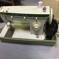 Early model Singer sewing machine with white and green metal body and control knobs