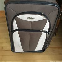 Large brown and beige suitcase with front zipper pockets and damaged handle base