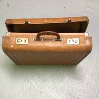 Top angle view of vintage children's suitcase showing brown hard shell, metal clasps, and brown handle.