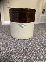 Front view of the 4 gallon Blue Crown crock showing brown and beige glazing with blue crown emblem and visible cracks.
