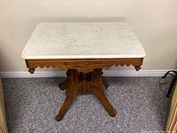 Full view of the rectangular white marble top table with stained oak base against beige wall on carpet.