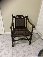 Front perspective of dark wood antique chair with woven rattan seat and detailed carved backrest.