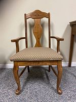 Front view of antique wooden chair showing carved backrest, armrests, and patterned reupholstered seat.