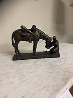Side angle of bronze statue showing cowboy kneeling and horse with saddle