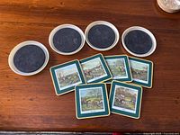 Photo showing nine coasters: four round beige border coasters with dark centers and five square green border coasters with countryside horse scene.