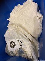 Folded white sheer plaid curtain fabric with visible metal rings inside a container