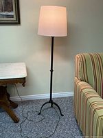 Full view of the floor lamp showing the lamp shade, lamp pole, and base with power cord on carpeted floor near furniture.