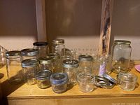 Overview of 16 assorted glass jars of varying heights and diameters, mostly with metal lids in gold, silver, and black.