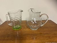 Two glass pitchers on wood table, showing wavy green base pitcher and round clear pitcher side by side.