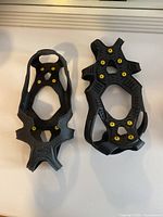 Pair of black rubber IceTrax ice cleats with yellow metal spikes laid flat on white surface, showing full views of both cleats.