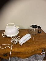 Lot showing white dome-shaped Superior electric kettle, white classic landline telephone, and clear glass coffee carafe on wooden surface
