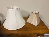 Two lamp shades on wooden surface: round white and beige square-shaped