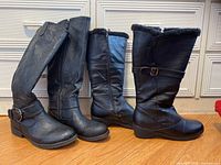 Four pairs of black leather boots of varying styles and heights, including mid-calf and knee-high lengths, shown side by side.