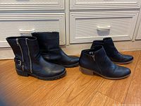Front view of two pairs of black leather boots side by side on floor, with white cabinets in background