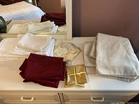 White, burgundy napkins, light linen napkins, white folded cloths, two trivets on dresser surface with mirror