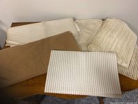 Four textured no-stick mats in white, beige, and brown colors shown on a wooden surface