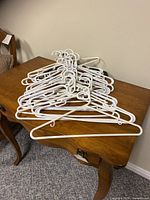 Stack of assorted white plastic hangers piled on a wooden table, showing their shape and condition clearly.