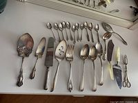 Full assortment of 20 assorted silver plated serving utensils laid out on table showing variety and style