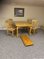 Full view of honey color wood dining table with four chairs and removable table leaf on carpeted floor.