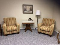 Two striped armchairs in a carpeted room with a small wooden table and floor lamp between them, showing full view of both chairs.