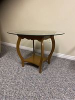 Front view of the vintage wooden end table with round glass top on carpeted floor against a wall.