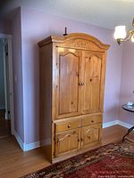 Front view of the solid pine wardrobe with honey stain finish, showing closed doors and drawer, traditional carved top detailing.