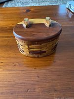 Closed view of small oval wicker jewellery box with wooden lid on wooden surface.