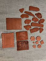 Photo shows 21 backless rubber stamps arranged on textured fabric. Various designs include flowers, architectural patterns, and textured rectangular shapes.