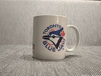 Front side of white ceramic mug showing Toronto Blue Jays vintage logo with blue jay bird and red maple leaf in baseball diamond.