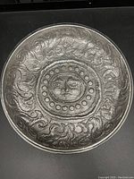 Top side view showing the embossed sun face at the center with surrounding circular patterns and swirling motifs on the platter surface.