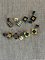 Six pairs of square cufflinks with blue and yellow geometric enamel designs on the front, displayed on fabric