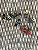 Three pairs of cufflinks laid on fabric background showing front geometric designs in black, red, blue, cream and silver.