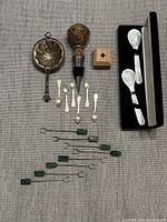 Overview of all items in the lot including sterling silver tea strainer, mother of pearl spoons, wood wine stopper with stand, green stone picks, and mini salt spoons.