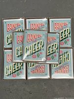 Photo showing nine unopened boxes of 'Bring on the Cheer' Christmas cards arranged on the floor.