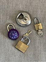 Photo showing four locks: silver disc lock, purple combination dial lock, brass Master padlock with keys, small brass padlock with key