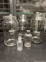 Front view of three clear Mason jars with two small glass bottles—one frosted and one clear, both with glass stoppers—placed in front of the jars