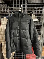 Front view of black Patagonia down jacket hanging on a metal grid, showing hood, zipper, and pocket placement