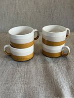 Four ceramic soup mugs arranged in two rows showing the white top half and brown bottom half with a thick horizontal brown band in the middle, each mug has a handle.