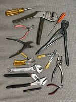 Various hand tools including wire strippers, pliers, adjustable wrenches, and screwdrivers laid out on a grey fabric background.