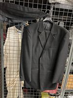 Photo of a black men's tuxedo jacket size 40 hanging on a black hanger against a metal grid, showing front view with notch lapels and pockets.