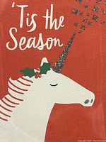 Close-up photo of card front showing white unicorn with glittery silver horn and holly decoration on red background with white 'Tis the Season' text.