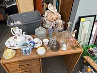 Wide view of assorted china and crystal displayed on wooden desk including teapot, pitchers, crystal candy dish, decanters, glasses, and handbells
